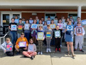 A group of students outside Hilltop Elementary holding artwork they created.